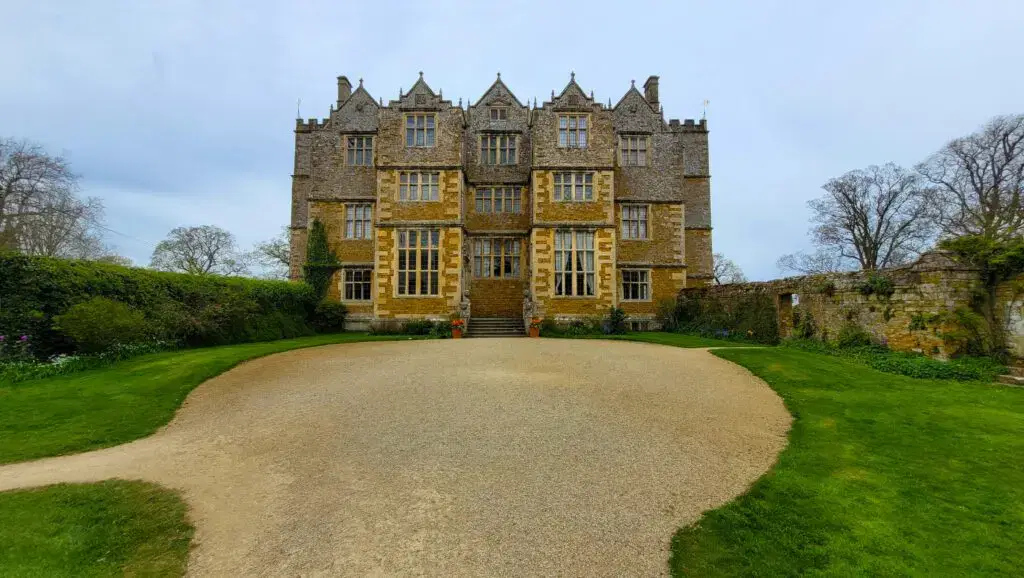 Grand manor house in the UK surrounded by blue sky, green grass and gravel.
