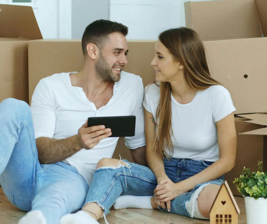 A young couple surrounded by packing boxes, looking happy with one another