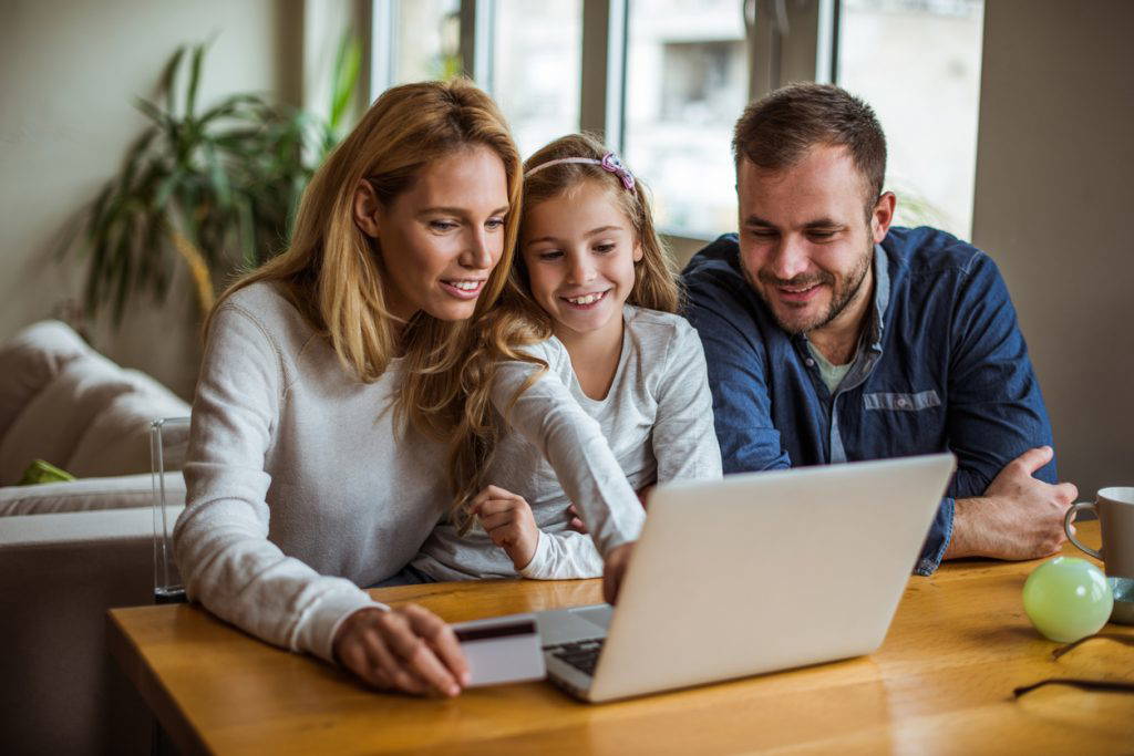 A couple with a small child huddled around a laptop.