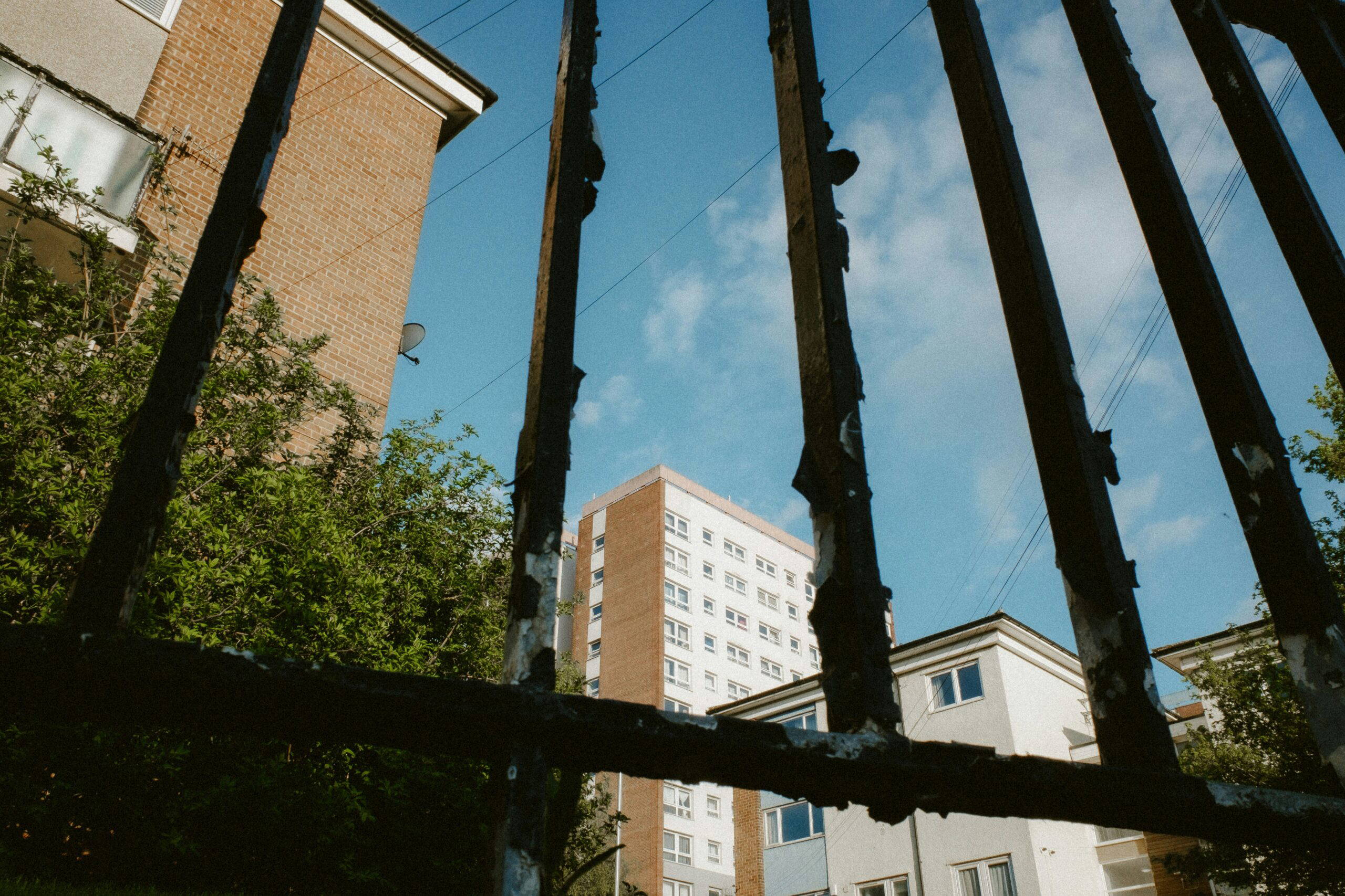 The view of a large block of flats, shot through the railings of a fence