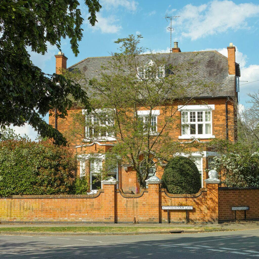 A large red brick family home in the UK with a large tree in the front garden